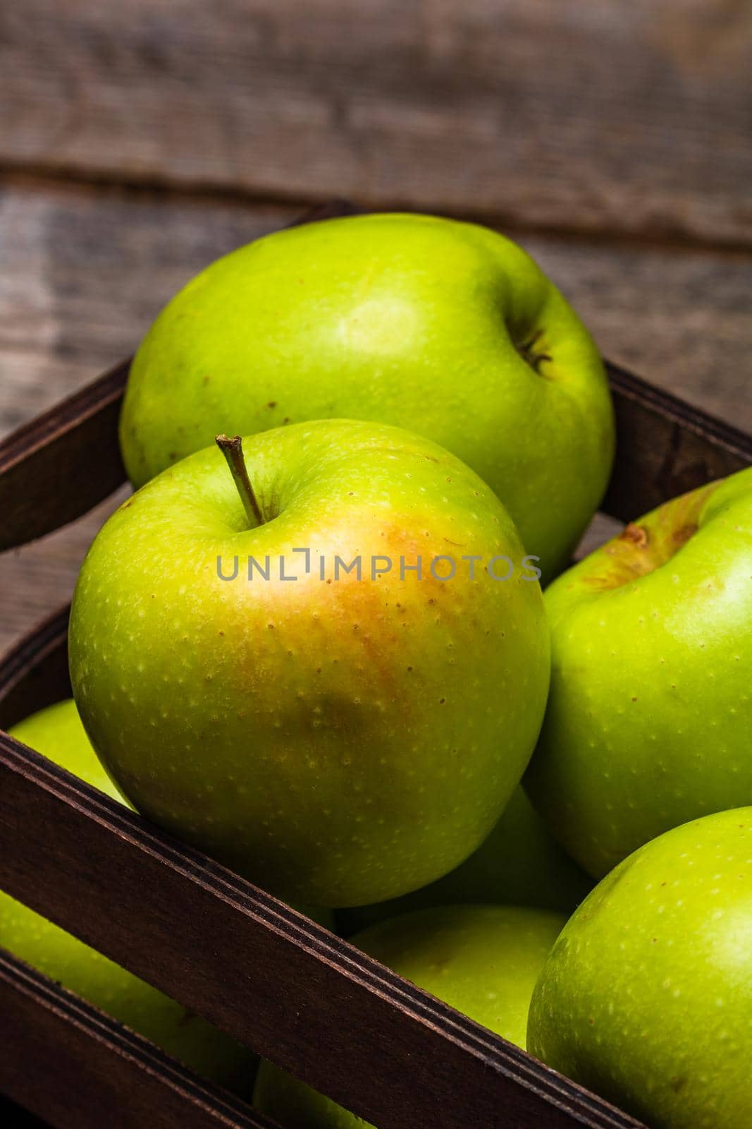 Wooden crate with ripe green apples on wooden table. by vladispas