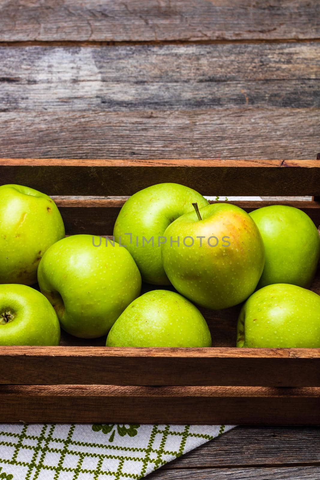 Wooden crate with ripe green apples on wooden table.