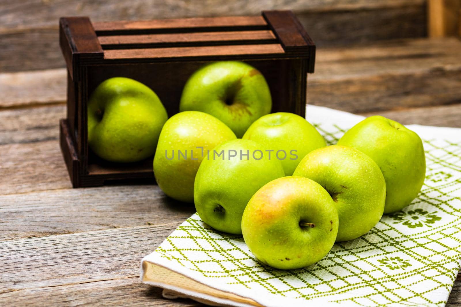 Wooden crate with ripe green apples on wooden table. by vladispas