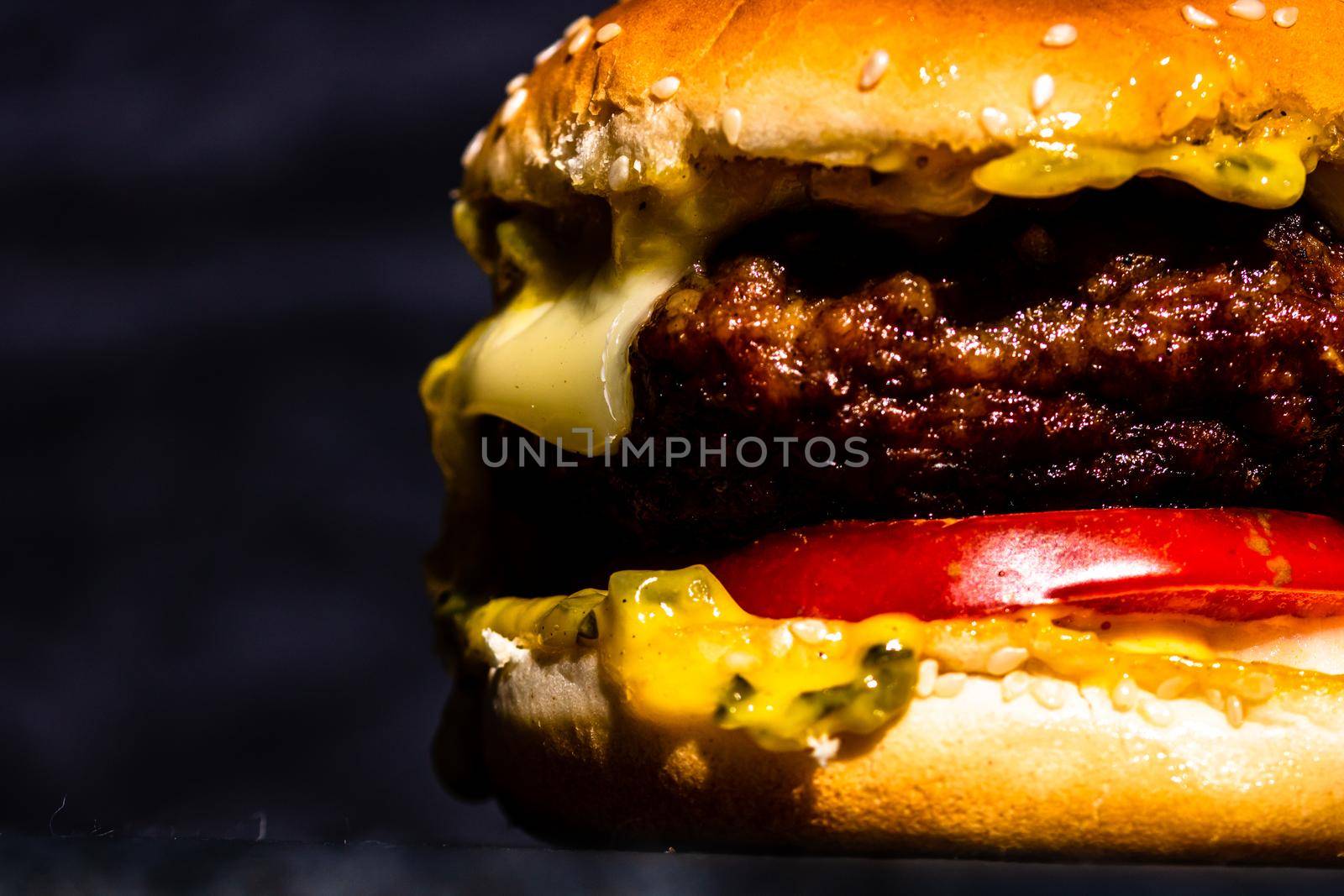 Juicy grilled beef cheeseburger isolated on black background. Cheeseburger with melted cheese on black stone plate. by vladispas