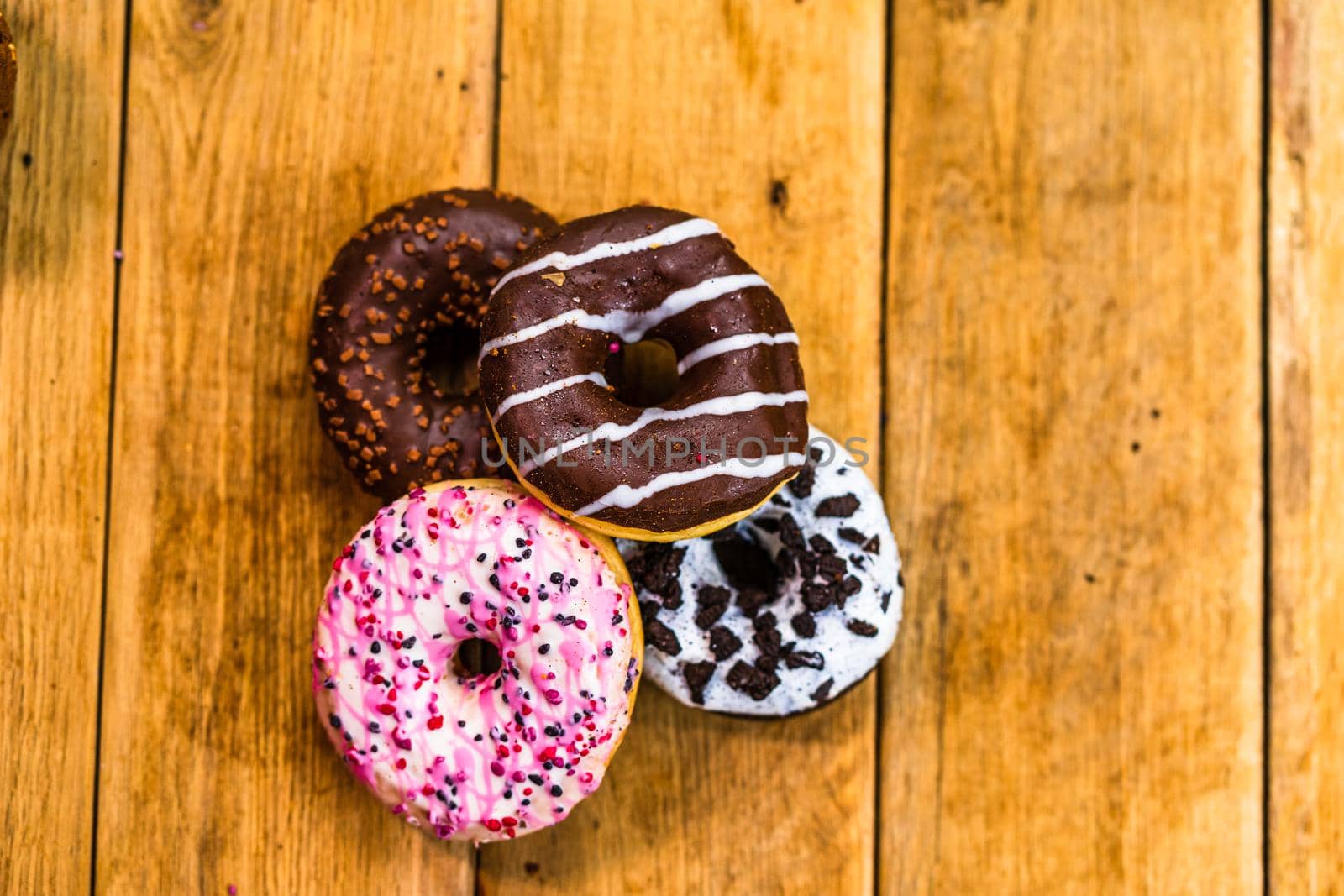 Colorful donuts on wooden table. Sweet icing sugar food with glazed sprinkles, doughnut with chocolate frosting. Top view with copy space