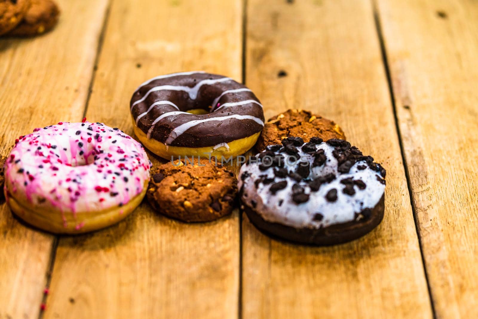 Colorful donuts on wooden table. Sweet icing sugar food with glazed sprinkles, doughnut with chocolate frosting. Top view with copy space