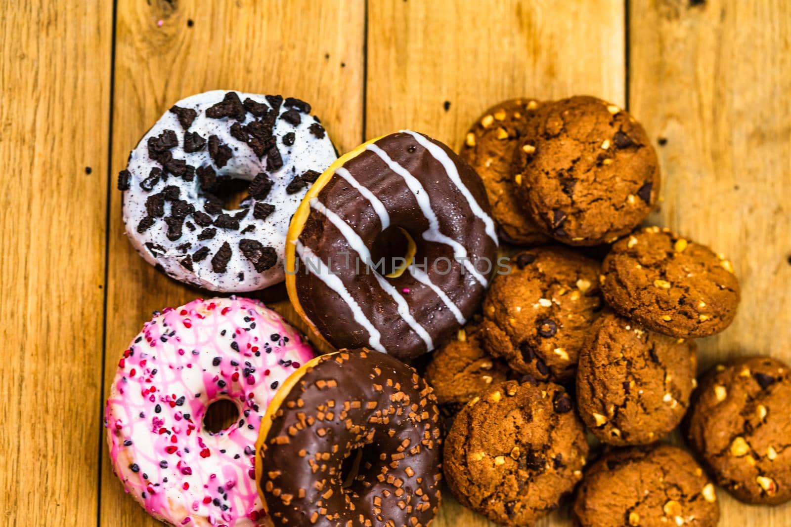 Colorful donuts and biscuits on wooden table. Sweet icing sugar food with glazed sprinkles, doughnut with chocolate frosting. Top view with copy space by vladispas