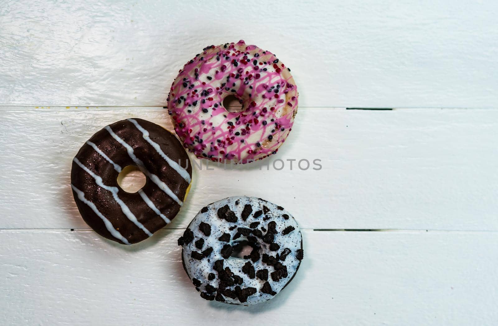 Colorful donuts on white wooden table. Sweet icing sugar food with glazed sprinkles, doughnut with frosting. Top view with copy space