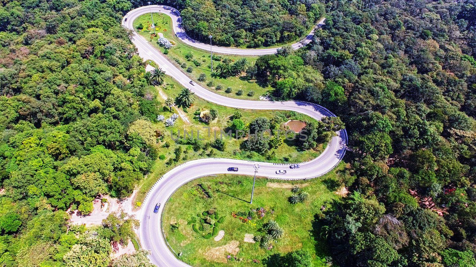 Aerial view from drone of cars are going through a curve road on the mountain with green forest. The transportation road across mountain. by Nuamfolio