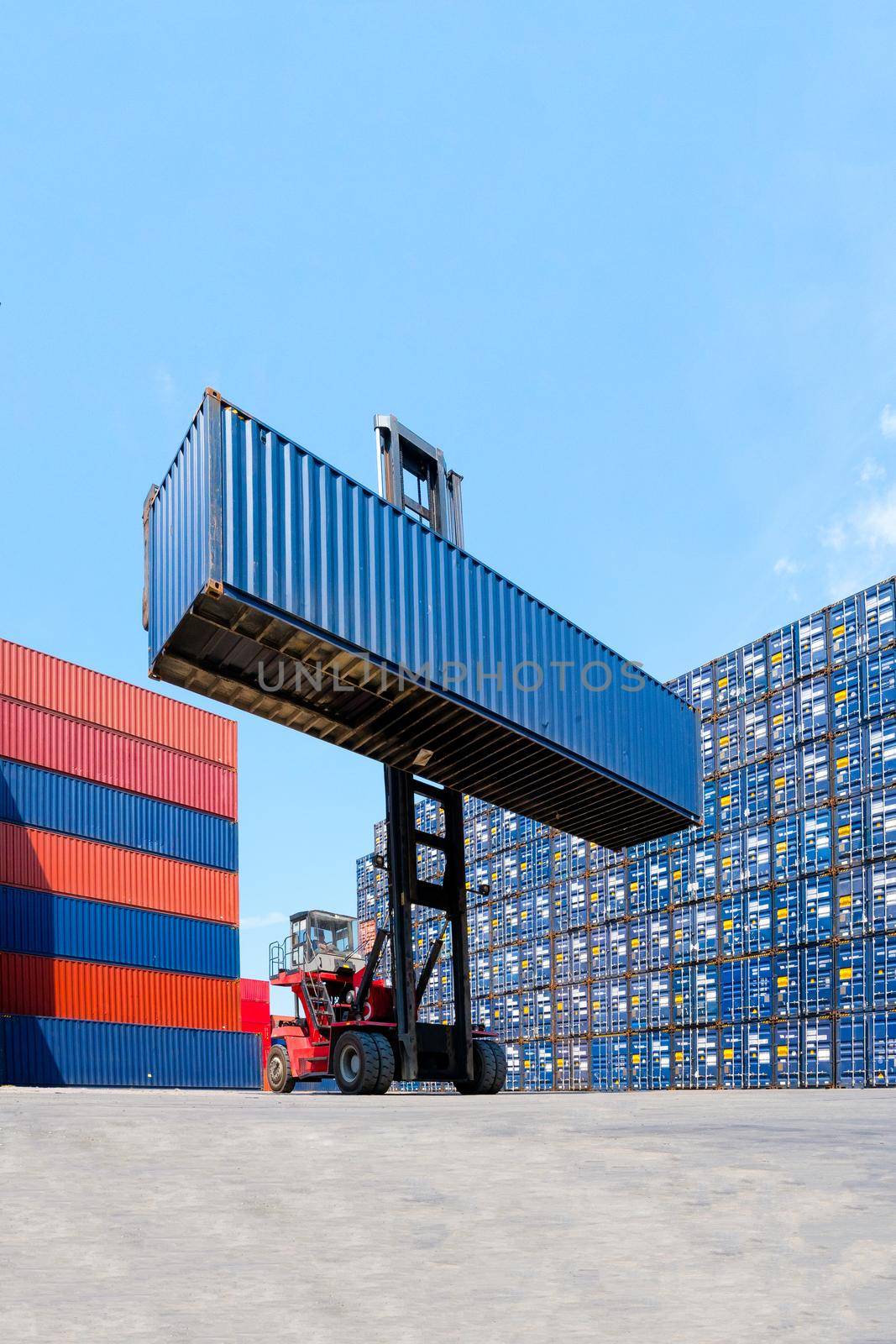 Forklift truck lifting cargo container in shipping yard or dock yard with cargo container stack in background for transportation import,export and logistic industrial concept.