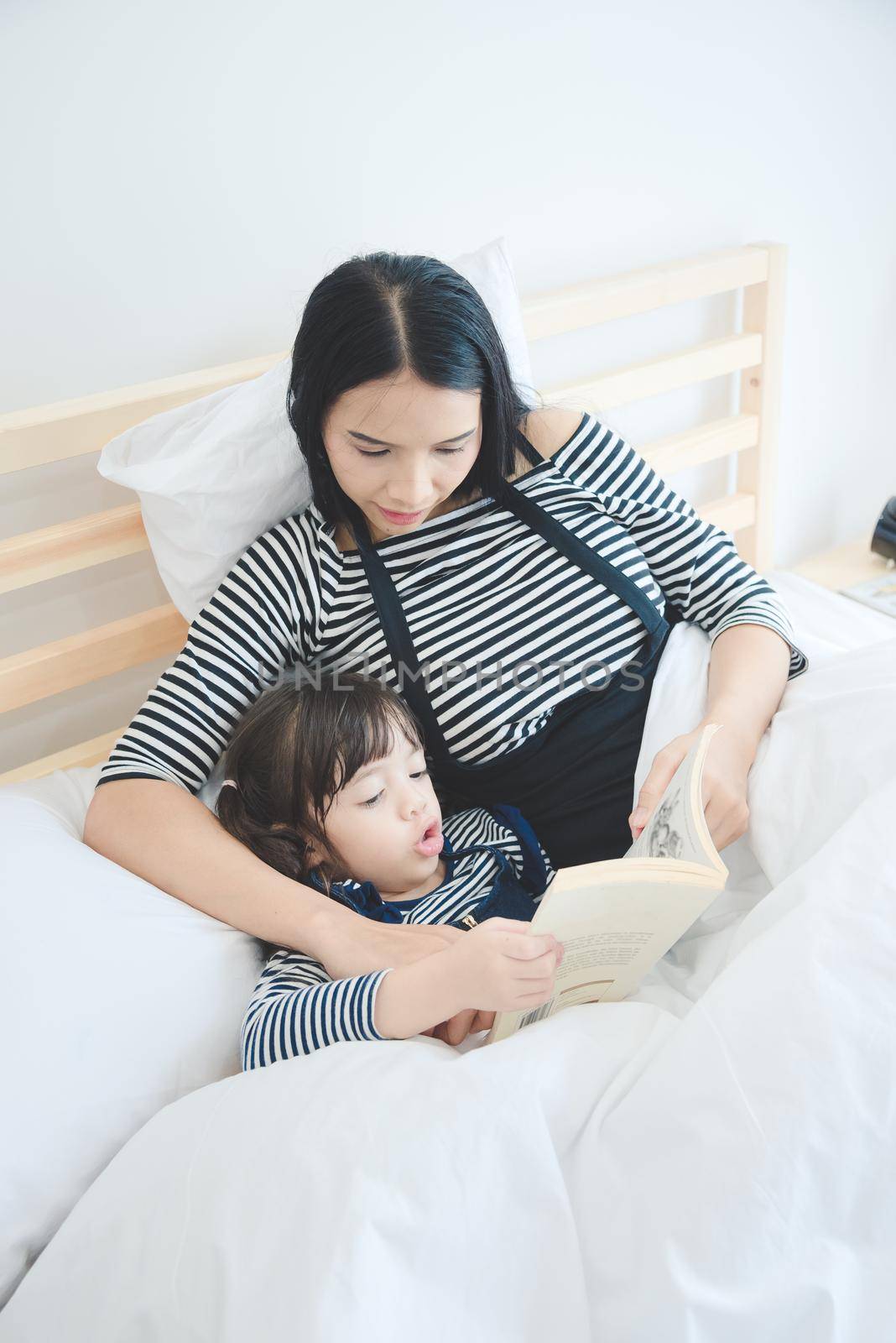 Happy loving family young asian mother teaching her daughter to reading a bed time story book in holiday.Photo design for family, children and happy people concept