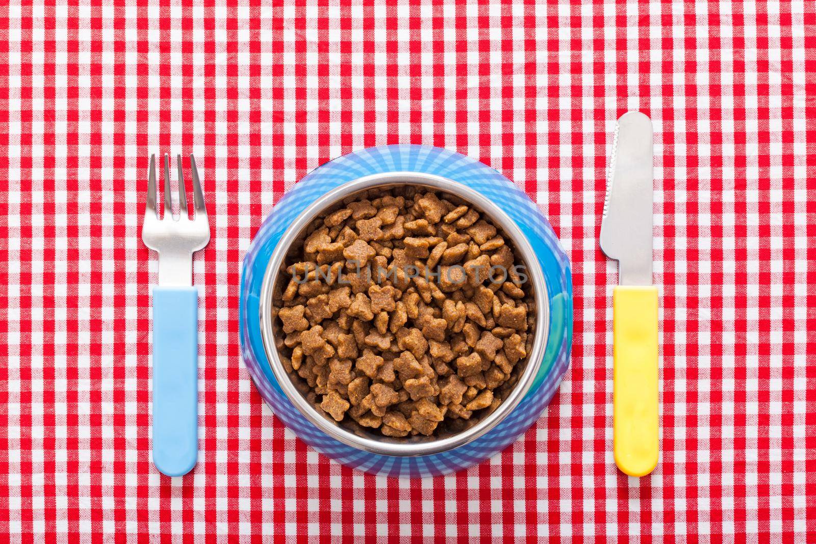 dog food bowl with knife and fork on tablecloth,full of dry food for pets