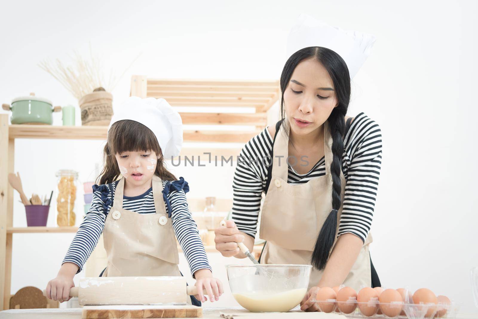 Asian mother and her daughter are preparing the dough to make a cake in the kitchen room on vacation. by Nuamfolio