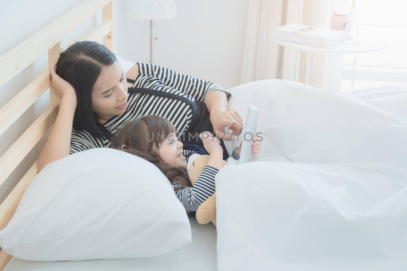 Happy loving family, asian young mother watching cartoon on smart tablet with her daughter in kid's room. Photo design for family, kids and happy people concept.
