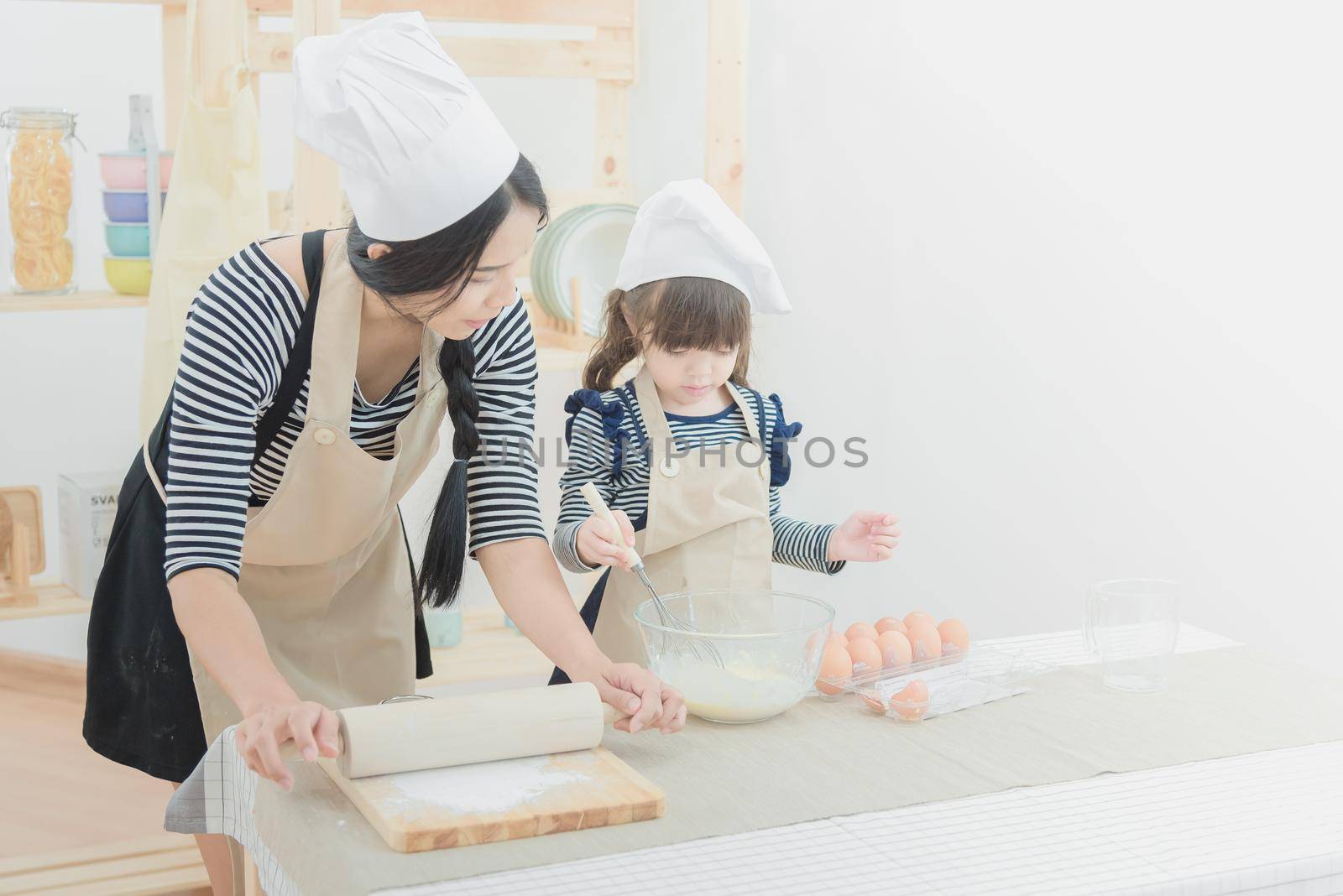 Happy family in the kitchen. Asian mother and her daughter preparing the dough to make a cake.Photo design for family, kids and happy people concept.