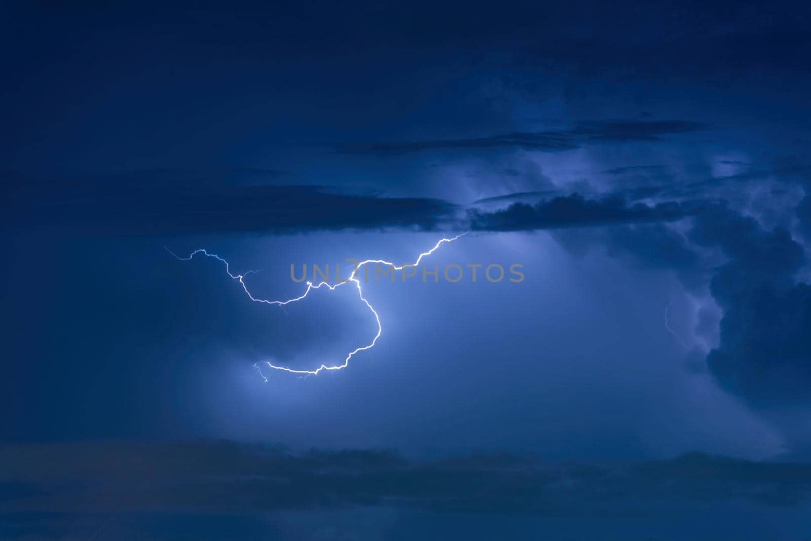 Thunder storm lightning strike on the dark cloudy sky background at night. by Nuamfolio