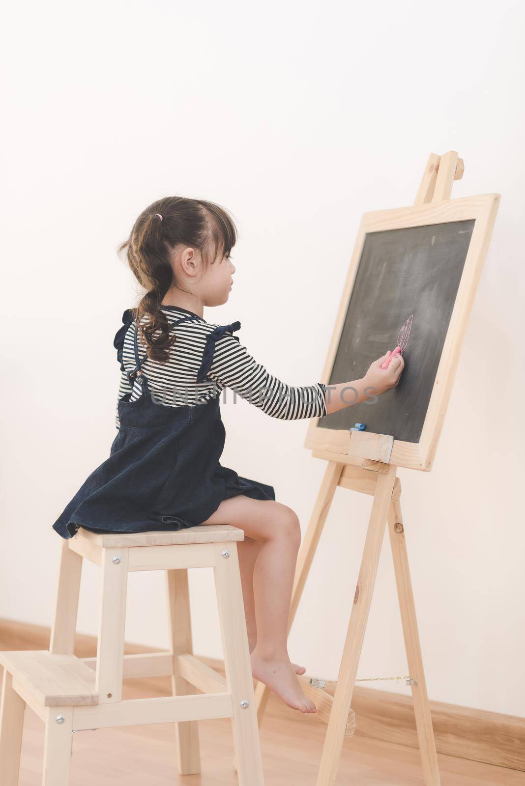 Happy asian girl kid draw cartoon with chalk on blackboard for learning at home. by Nuamfolio