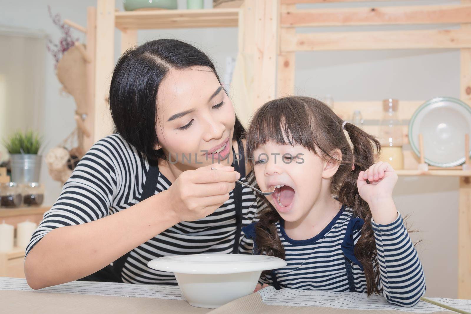 Happy family of asian mom feeding healthy breakfast to her cute daughter in the morning. Photo series of family, kids and happy people concept.