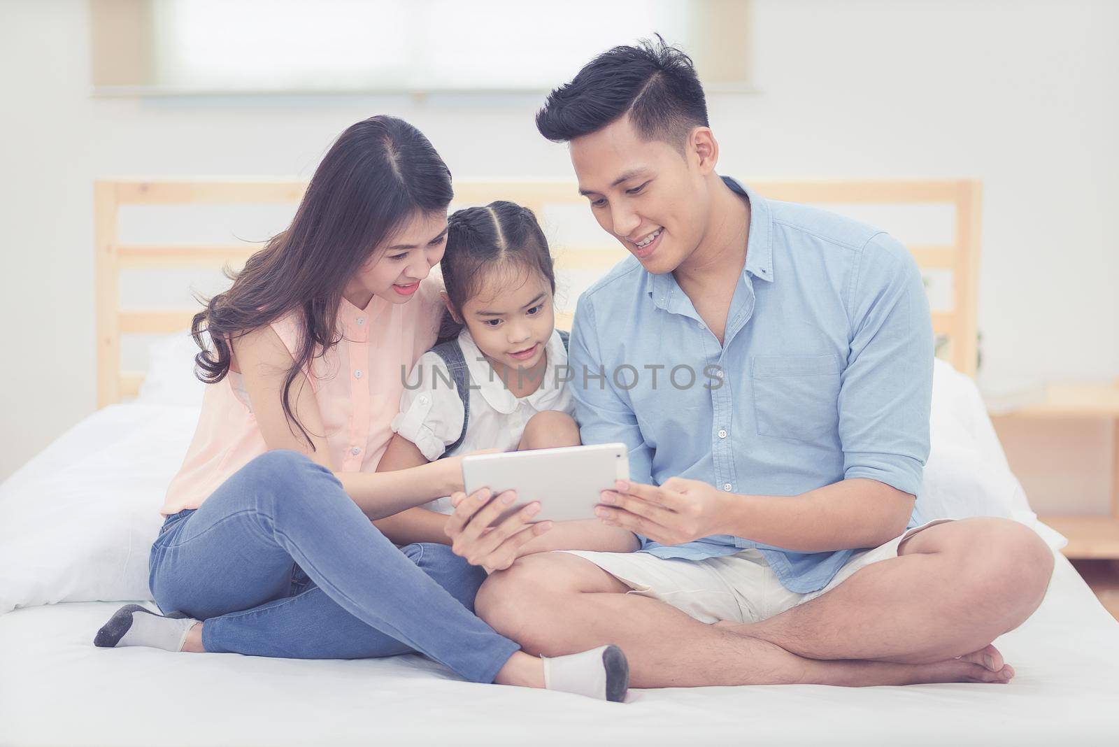Asian father and mother watching cartoon with daughter on smart tablet together at home.Photo series of family, kids and happy people concept.
