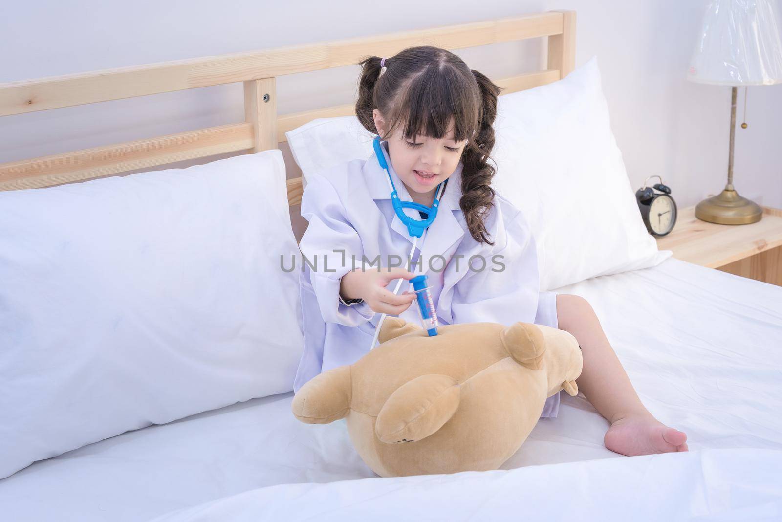 Cute asian little girl enjoy playing doctor with doctor toy set and cute doll at home by Nuamfolio