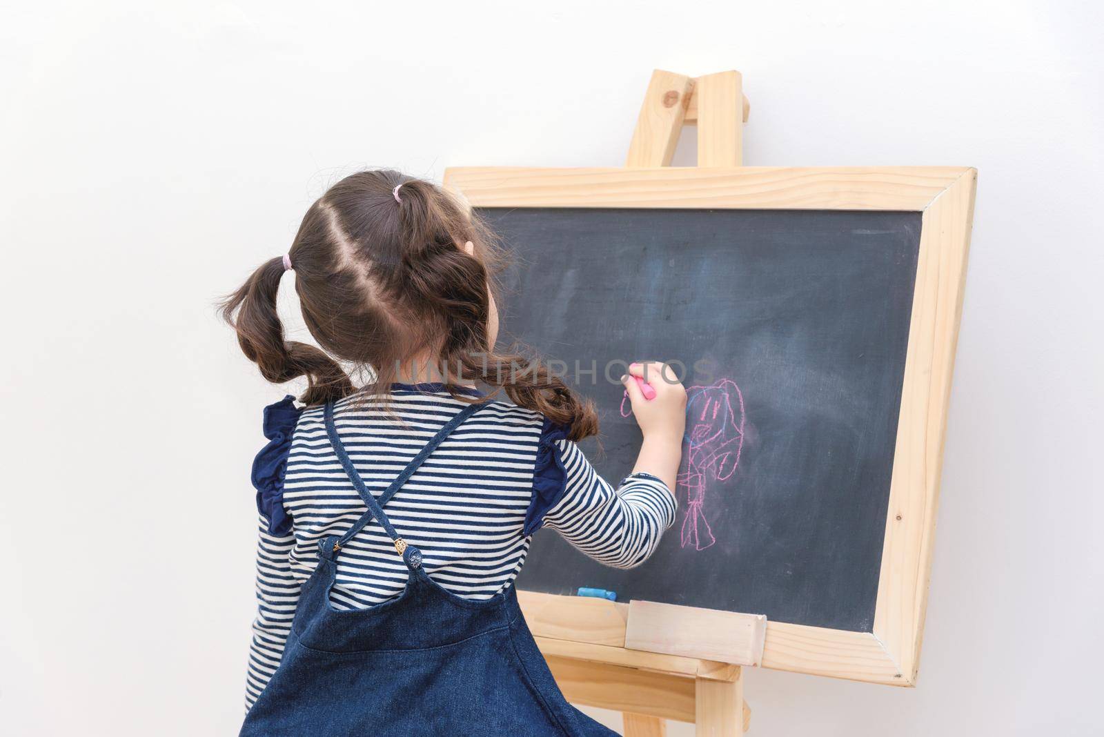 Happy asian girl kid draw cartoon with chalk on blackboard for learning at home. Photo for kid education and school study concept.