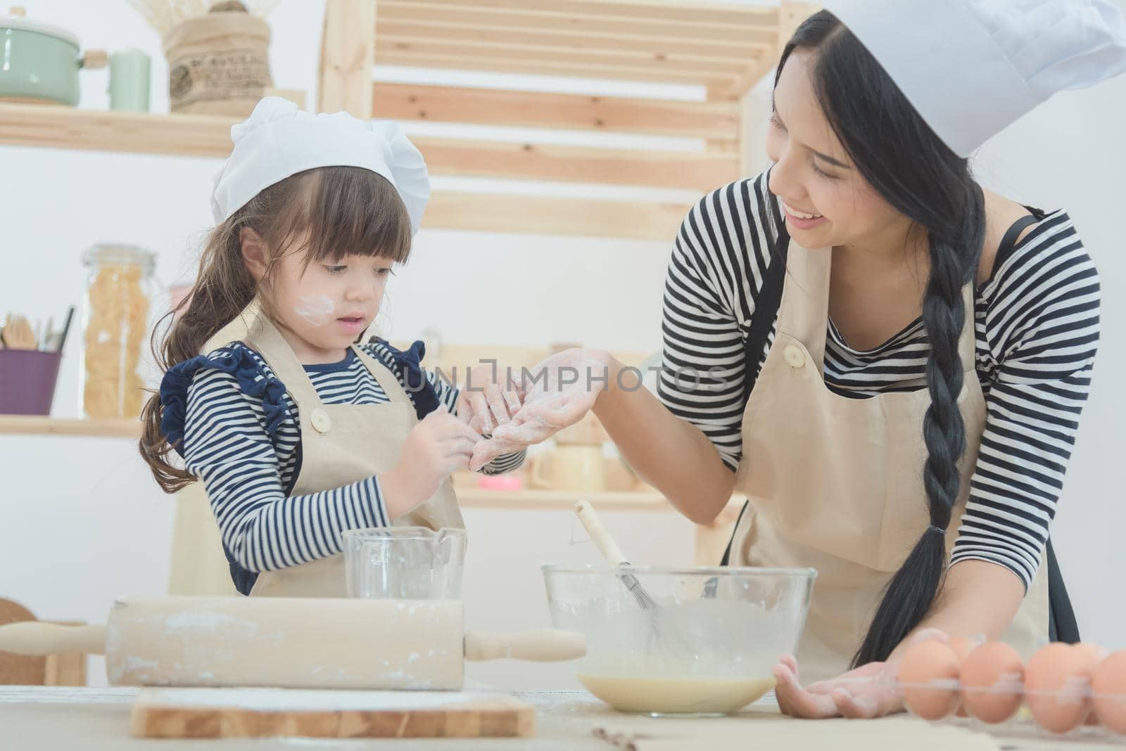 Happy loving family mother and her daughter cooking together to make a cake in kitchen room.Photo design for family, kids and happy people concept
