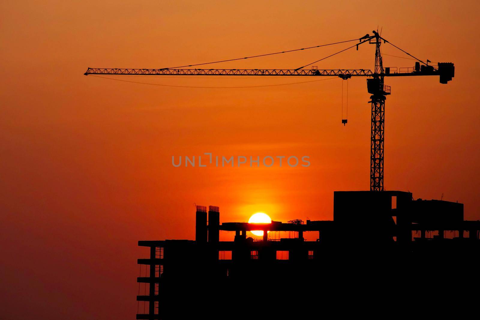 Silhouetted construction crane and building at construction site on sunset for construction industrial work concept
