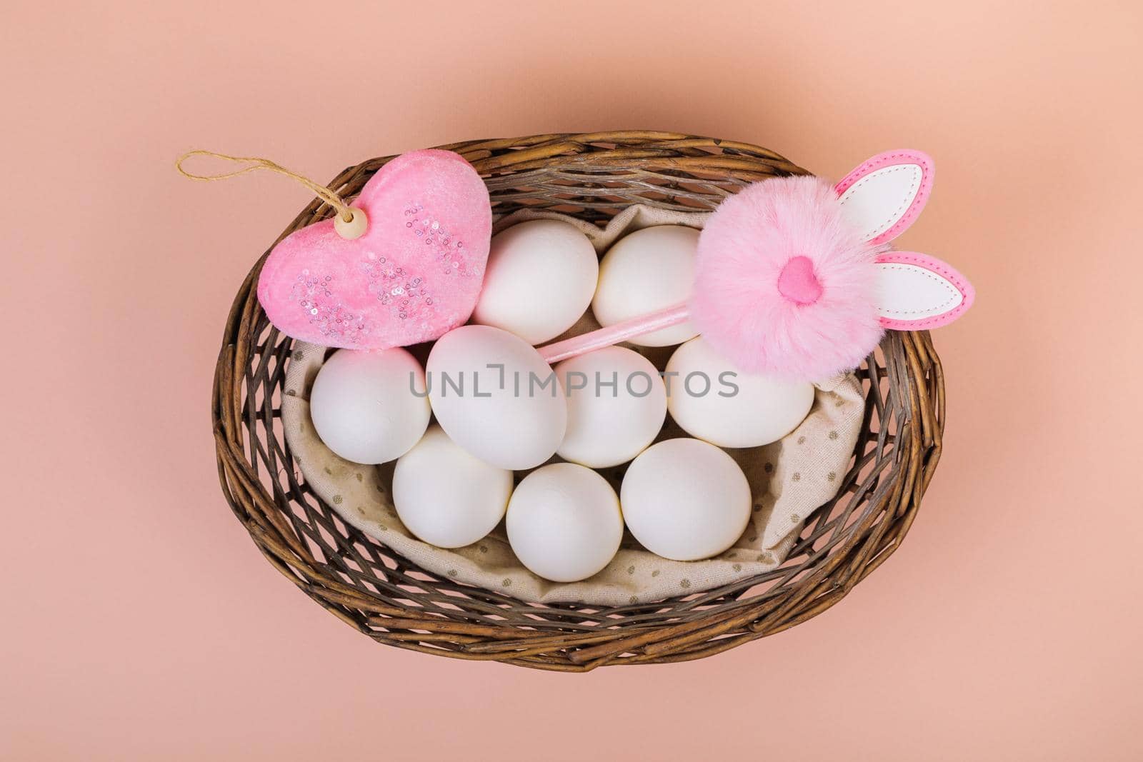 Easter. White eggs in a basket with an artificial rabbit, on a uniform pink background. Place for text.