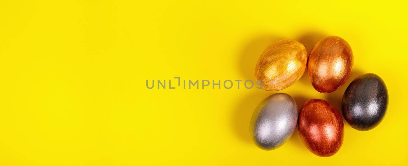 Easter. Multi-colored eggs on a uniform yellow background with place for text. View from above. Banner