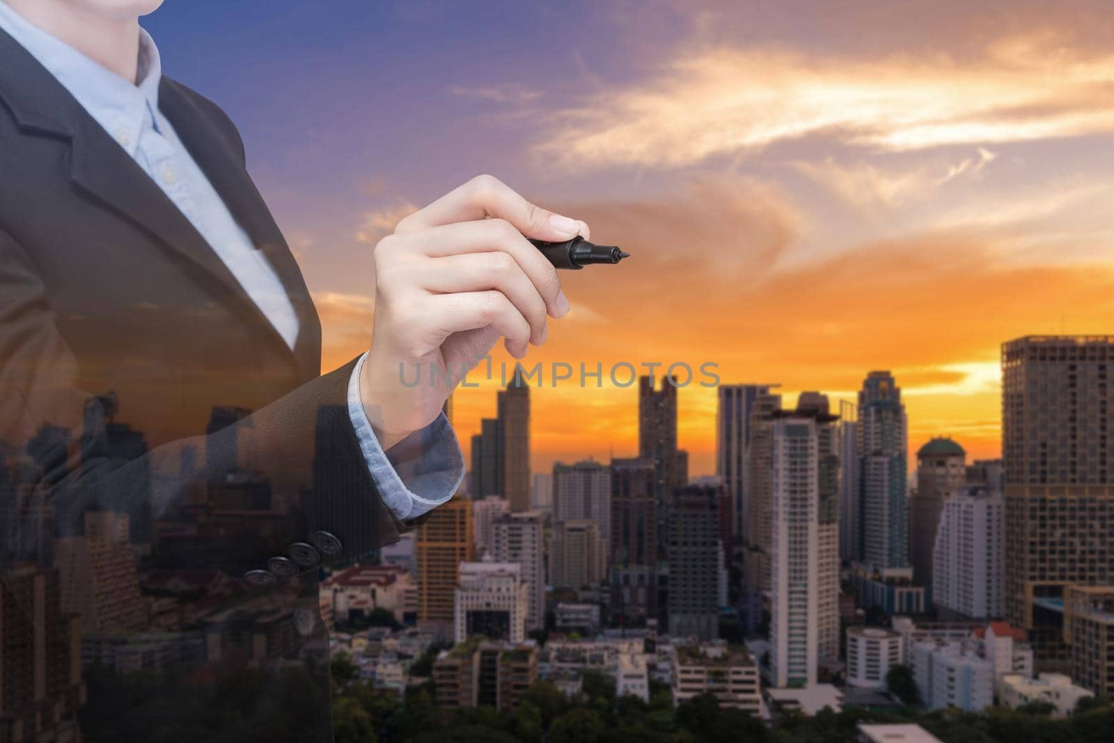 Double exposure Young and Smart business woman holds a marker writing in air with real estate building in background. Elegant Design for smart business and smart technology concept by Nuamfolio