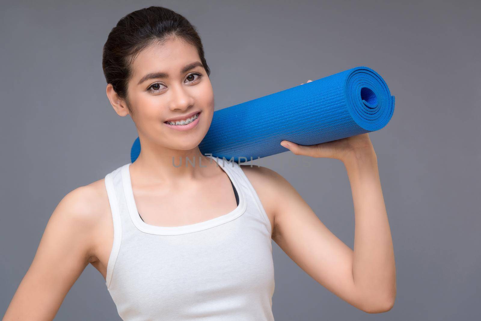 Young asian woman with happy smile holding her yoga mat at yoga healthy sport gym. Yoga and meditation have good benefits for health. Photo concept for Yoga Sport and Healthy lifestyle. by Nuamfolio