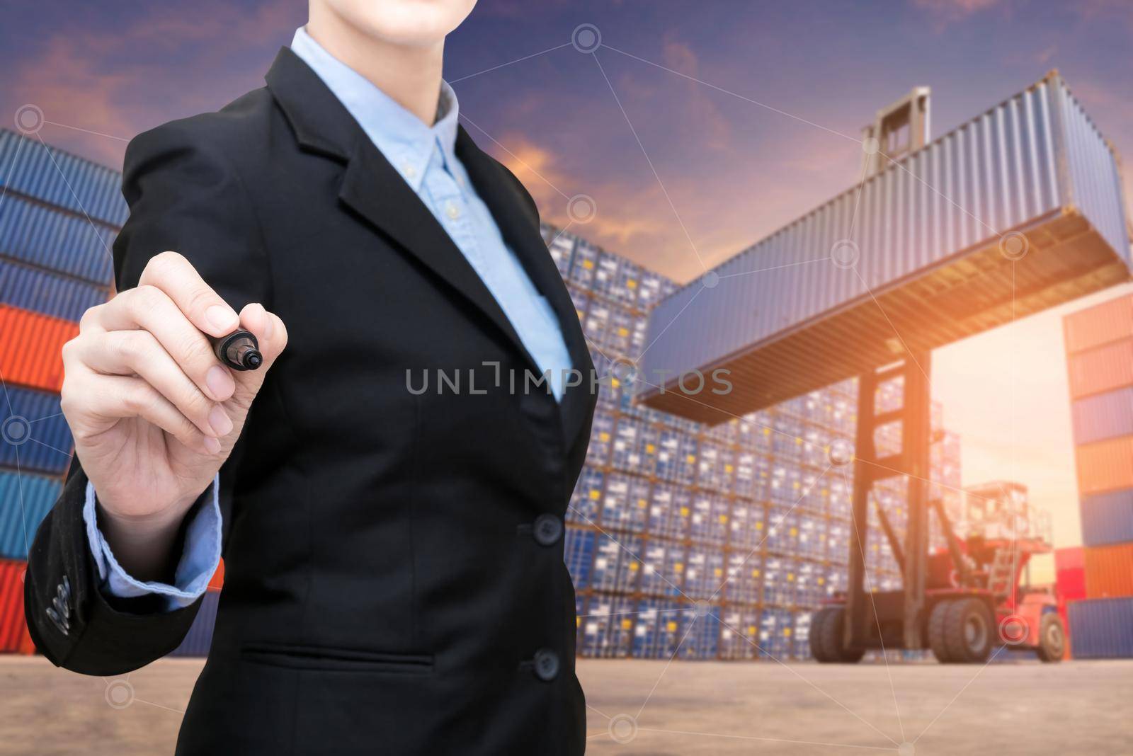 Smart Business woman holds a marker writing with copy space and Forklift truck lifting cargo container in shipping yard in background for transportation import,export and logistic industrial concept by Nuamfolio