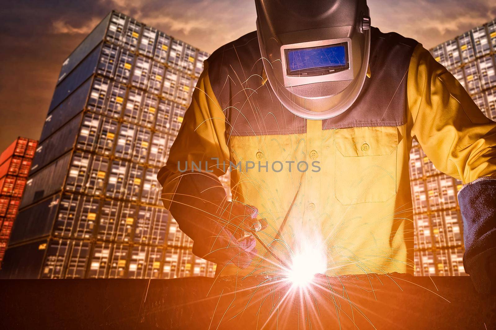 Industrial welding worker with safety equipments and protective mask welding steel structure with cargo container stack in background for transportation import,export and logistic industrial concept