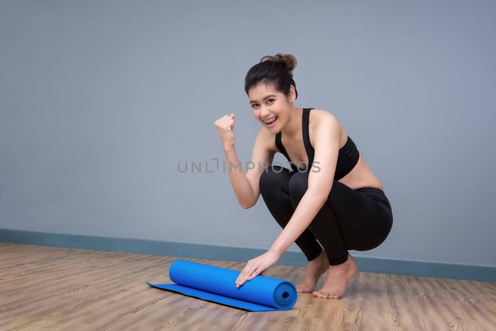 Young asian woman with happy smile preparing yoga mat at yoga healthy sport gym. Yoga and meditation have good benefits for health. Photo concept for Yoga Sport and Healthy lifestyle. by Nuamfolio