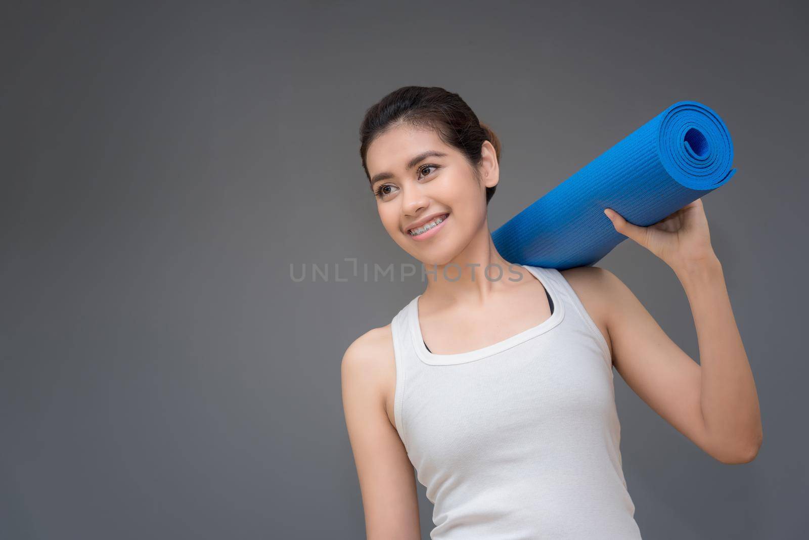 Young asian woman with happy smile holding her yoga mat at yoga healthy sport gym. Yoga and meditation have good benefits for health. Photo concept for Yoga Sport and Healthy lifestyle.