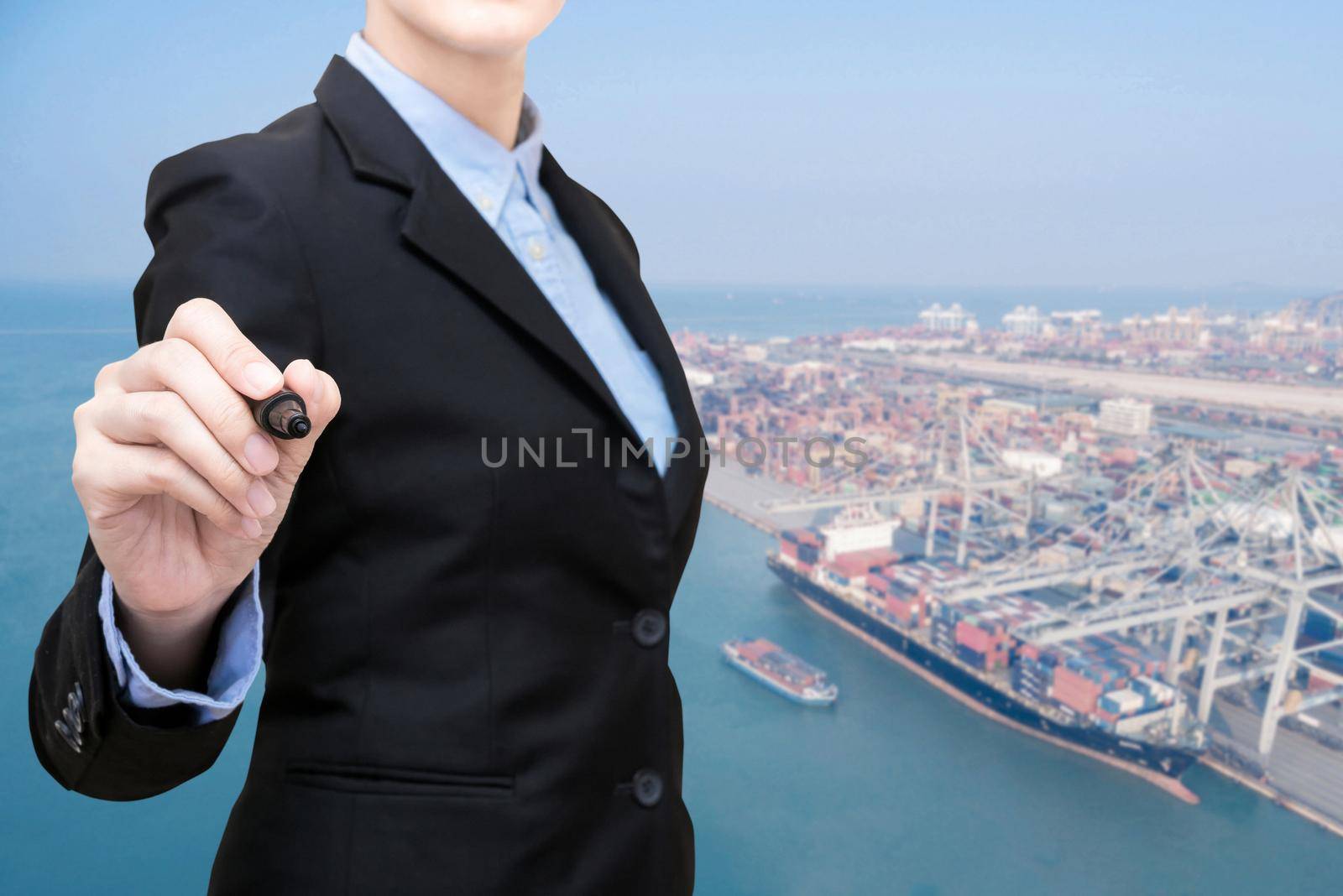 Business woman writing with container shipping boat at shipping yard in background.Photo concept for transportation of cargo shipping container Logistic,Import and Export industry.