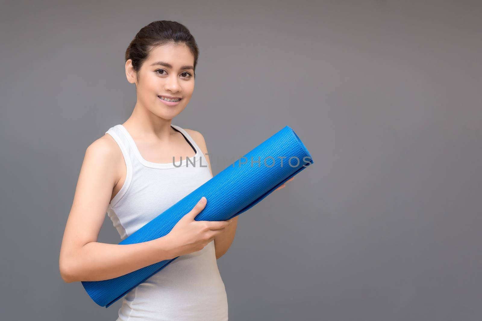 Young asian woman holding her yoga mat at yoga healthy sport gym. Yoga and meditation have good benefits for health. Photo concept for Yoga Sport and Healthy lifestyle