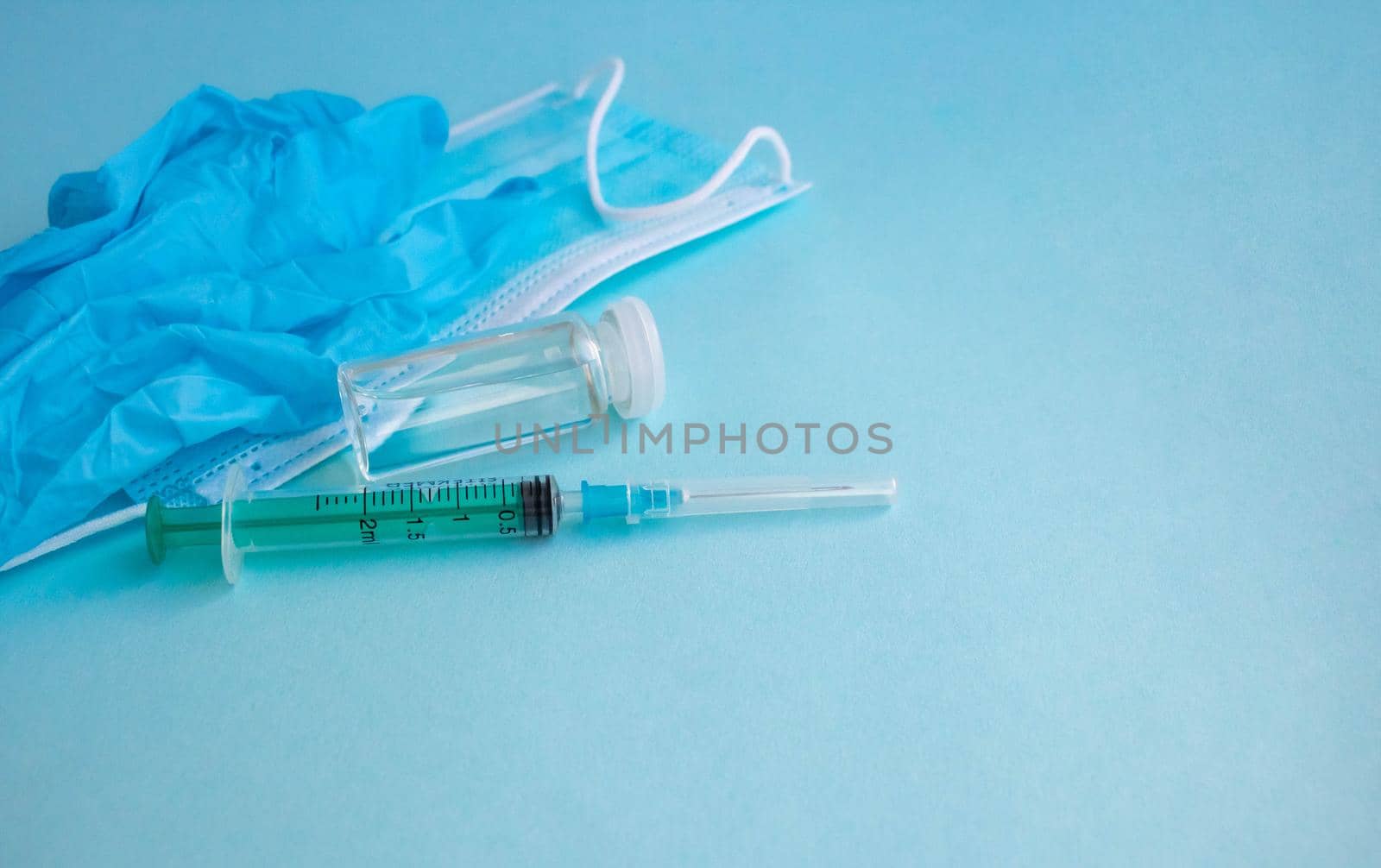 A syringe, gloves, mask, and a bottle of vaccine stand on a blue background. For the prevention, immunization and treatment of coronavirus infection. The concept of medicine and health care.
