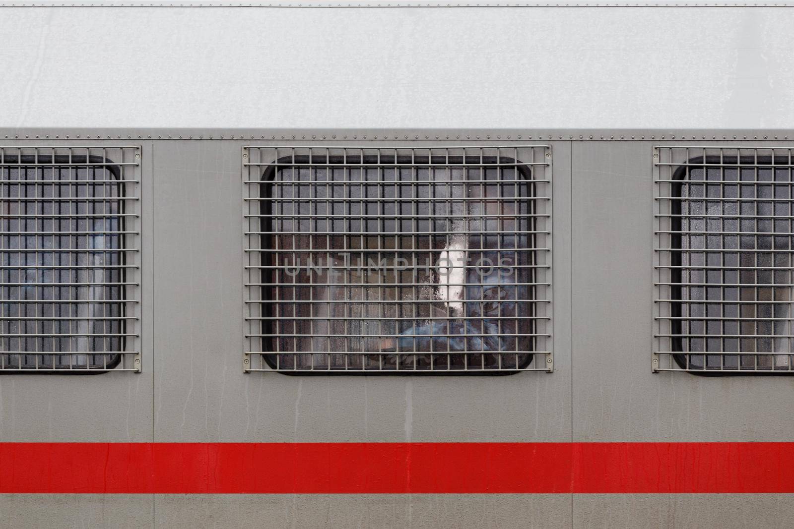 russian national guard officer inside of riot police truck window behind metal grate.