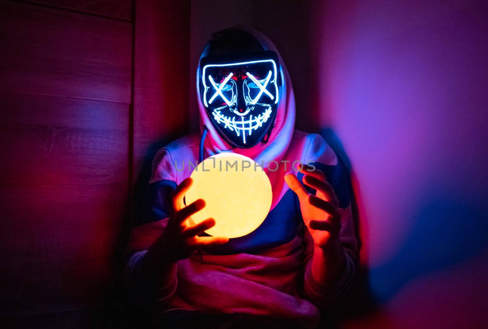 Man in glowing mask sitting in the corner with moon-shaped lamp 