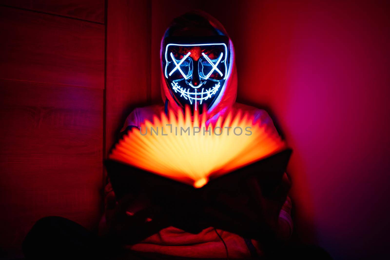 Man in glowing mask sitting in the corner with book-shaped lamp  by Wierzchu