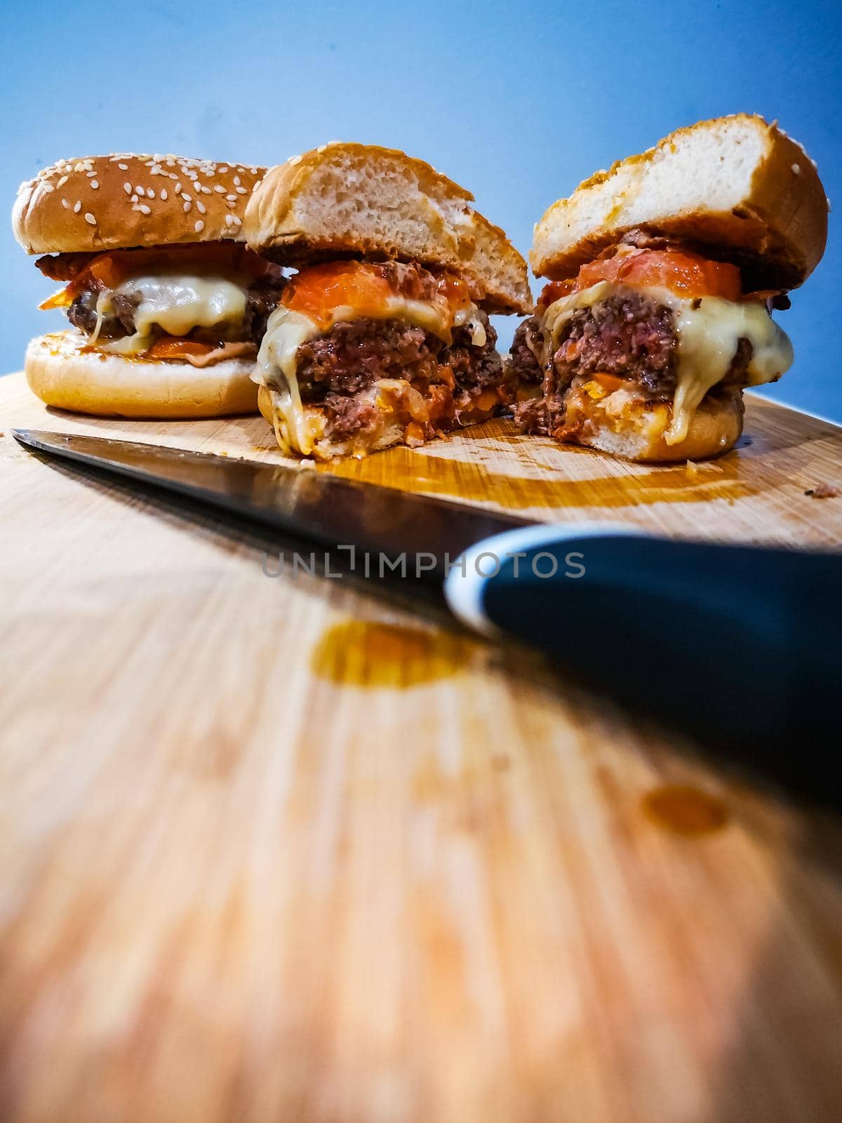 Black knife in front of burgers with beef cheese tomato and bacon