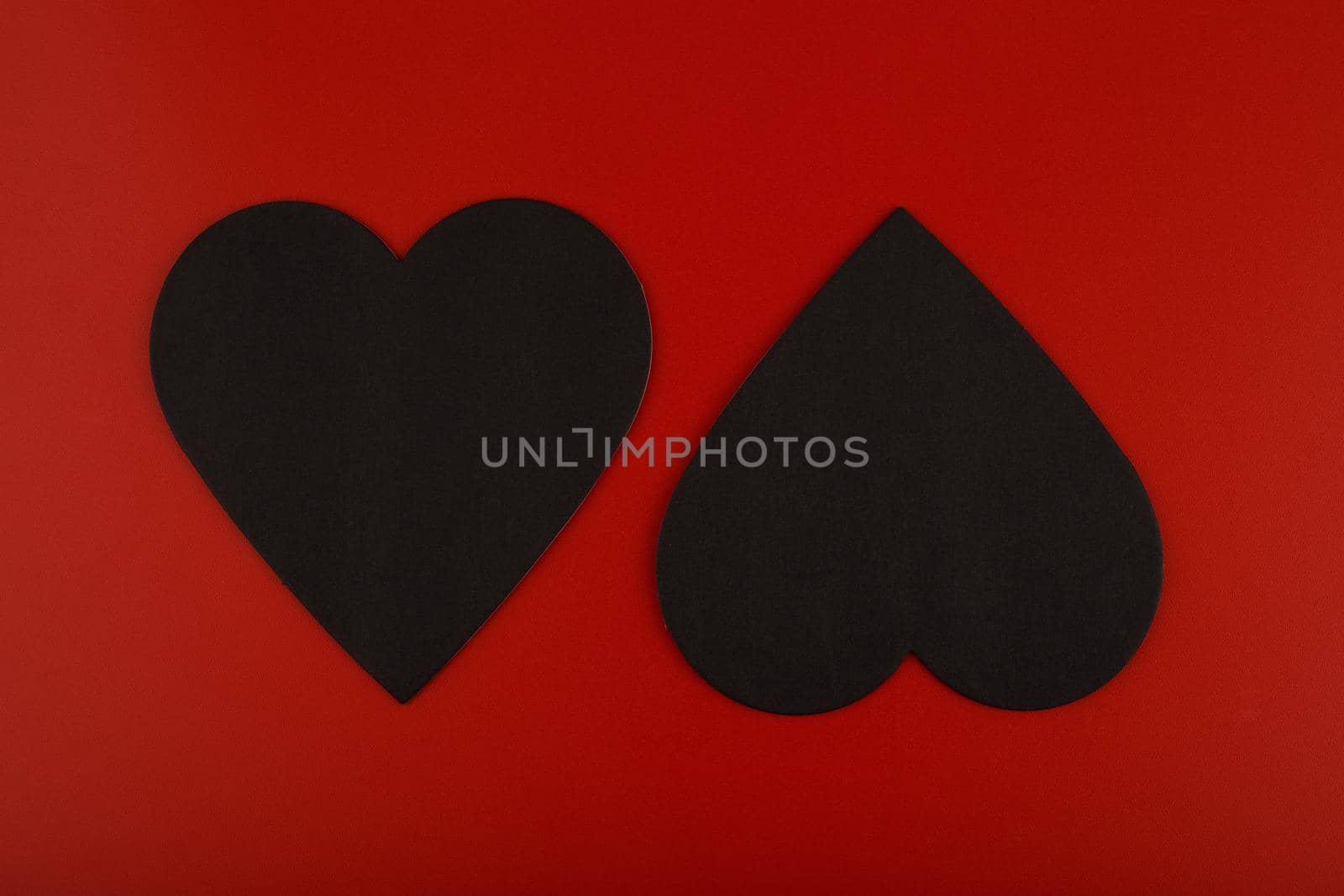 Top view of two black paper hearts against red background. Concept of love and St. Valentine's day