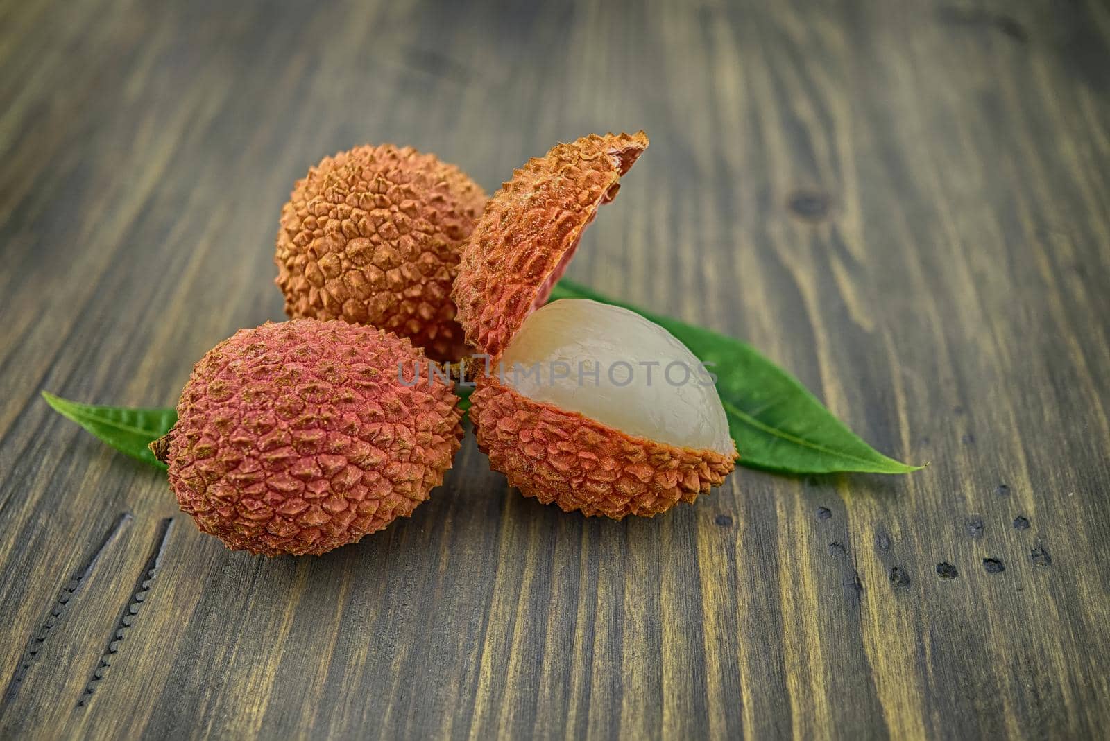 Lychee fruit whole and opened with green leaves decoration on rustic wood background