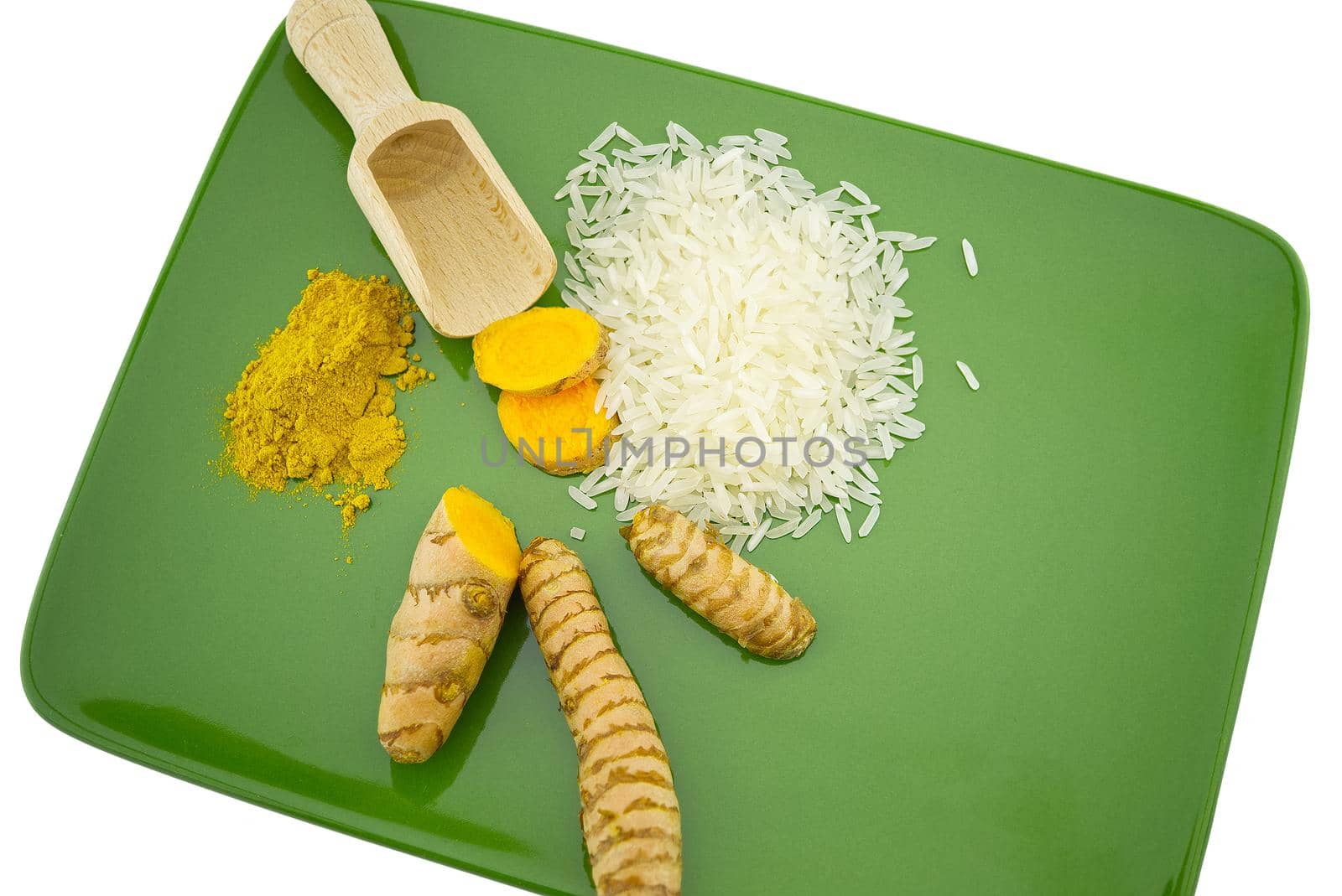 Fresh raw turmeric roots and slices next to heaps of rice and spice powder on a green plate with free space for text