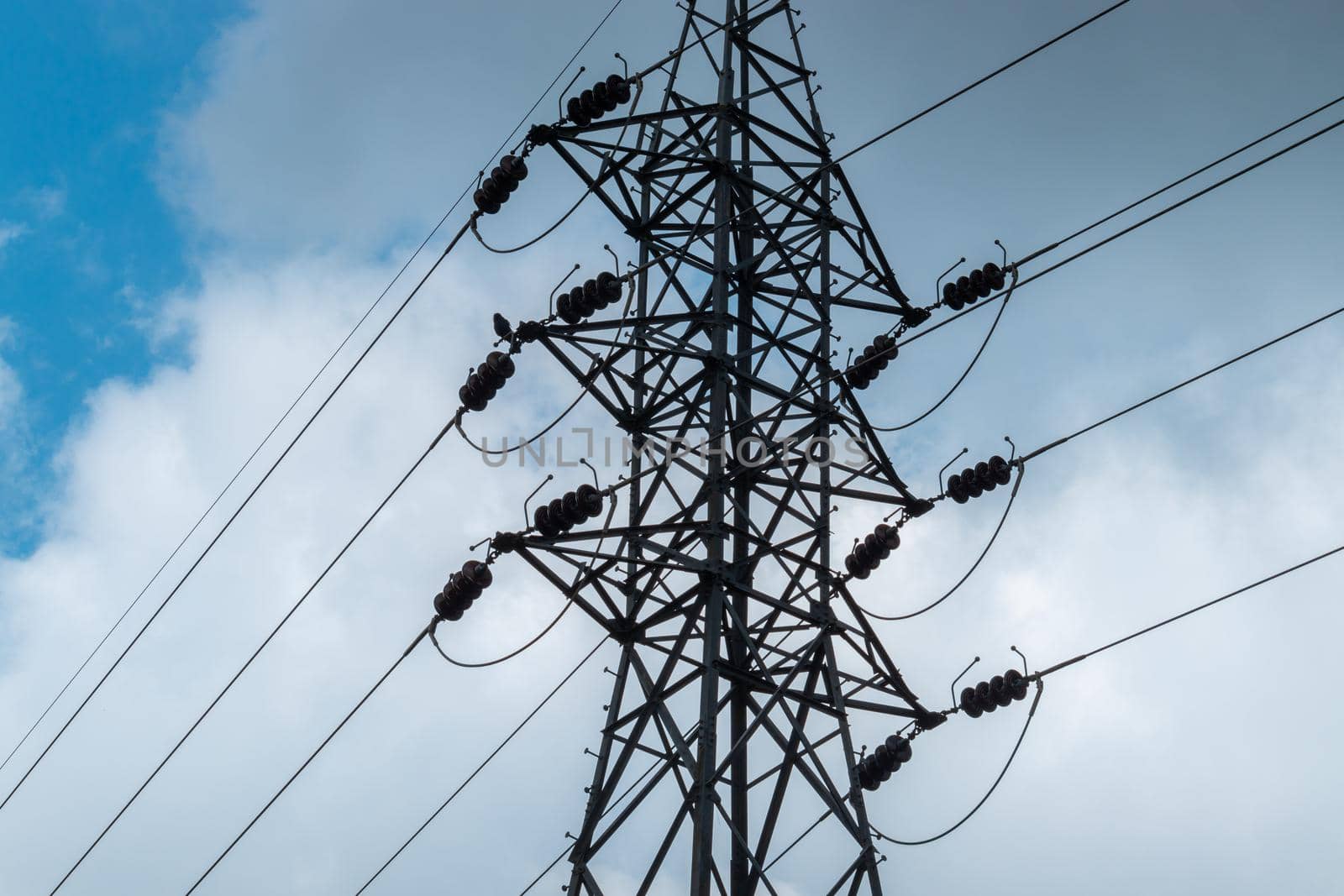 High voltage Electric tower pole silhouette and power lines against dark bloomy grey clouds. by nilanka