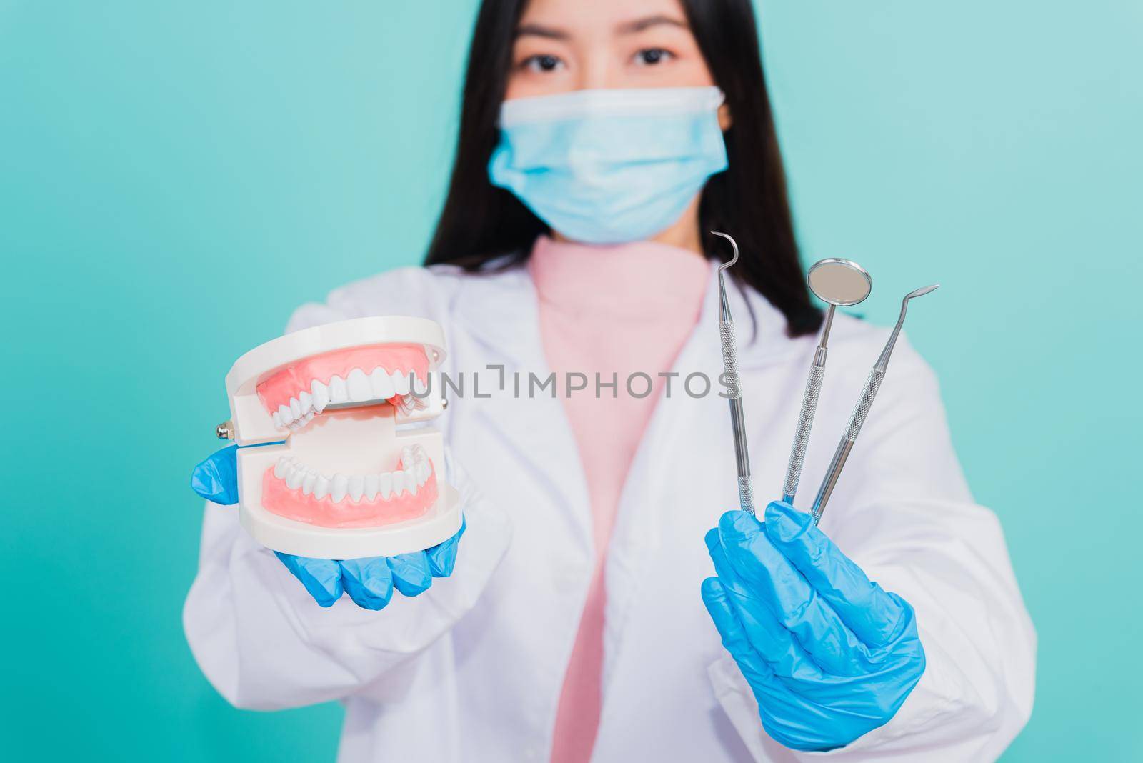 Asian beautiful woman dentist holding professional tool and model teeth denture, female doctor checking denture studio shot isolated on blue background. Dental hygiene surgery health care concept