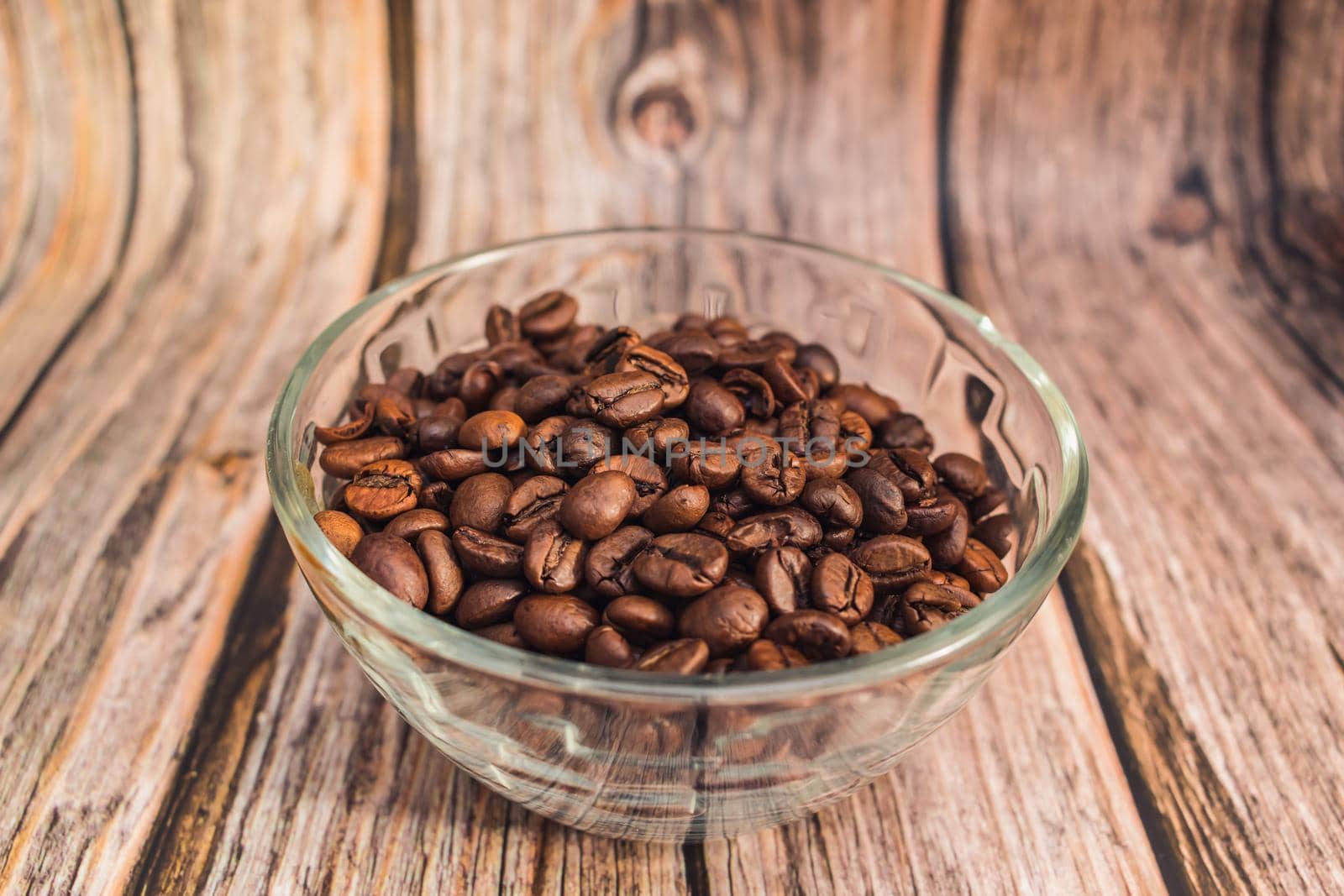 Freshly roasted coffee beans lie in a transparent glass vase on a wooden table