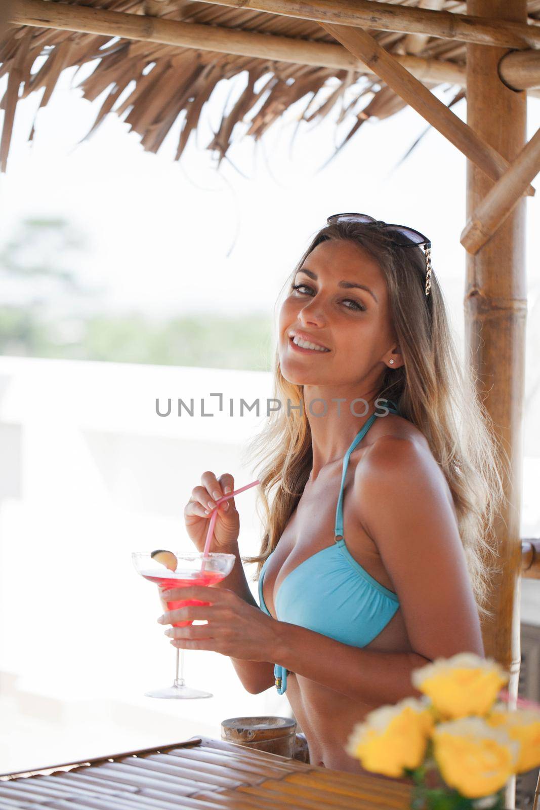 Woman in bikini drinking cocktail in summertime on beach bar