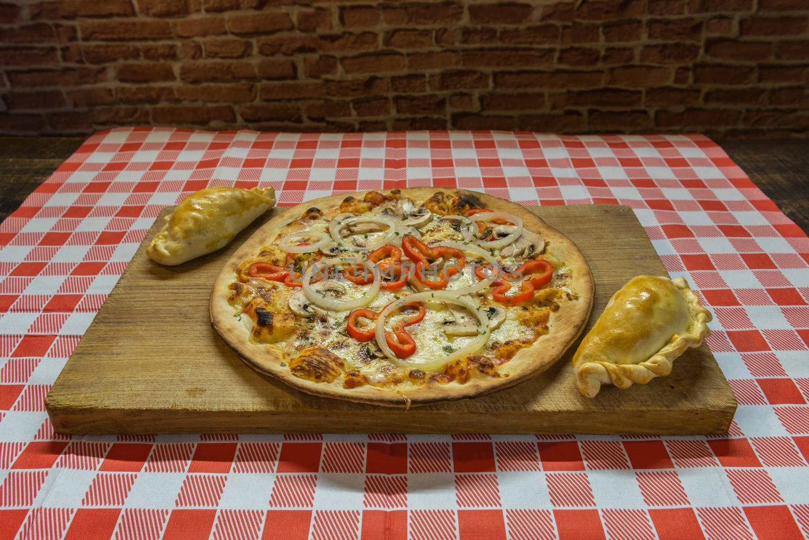 Traditional baked Argentine and Uruguay empanadas savoury pastries with meat beef stuffing against wooden background and pizza whit onion and red peppers.