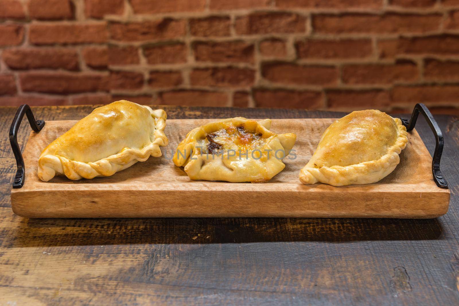 Traditional baked Argentine and Uruguay empanadas savoury pastries with meat beef stuffing against wooden background.