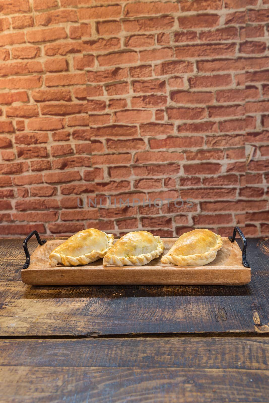 Traditional baked Argentine and Uruguay empanadas savoury pastries with meat beef stuffing against wooden background.