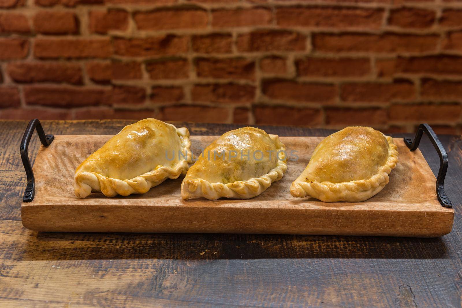 Traditional baked Argentine and Uruguay empanadas savoury pastries with meat beef stuffing against wooden background.