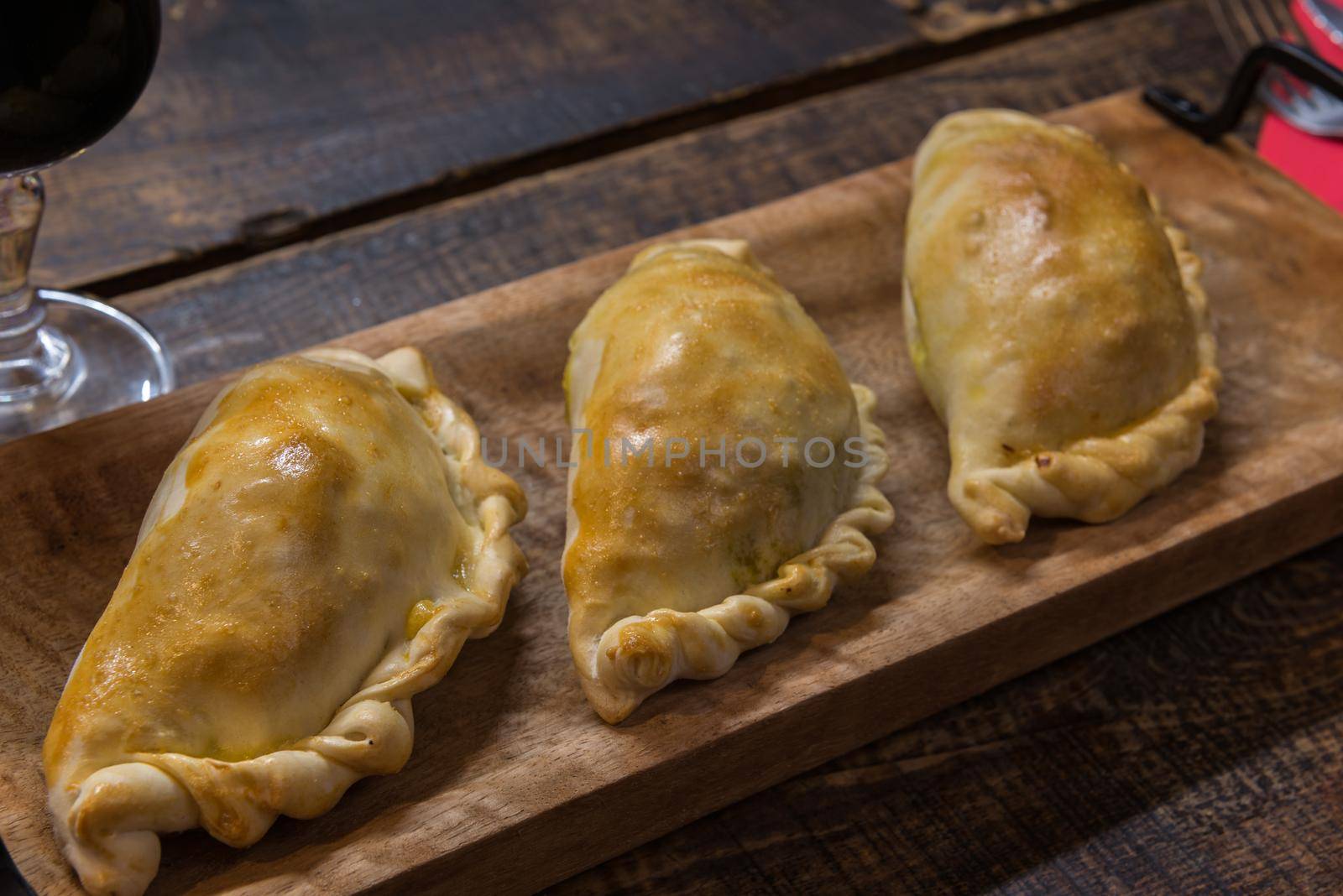 Traditional baked Argentine and Uruguay empanadas savoury pastries with meat beef stuffing against wooden background.